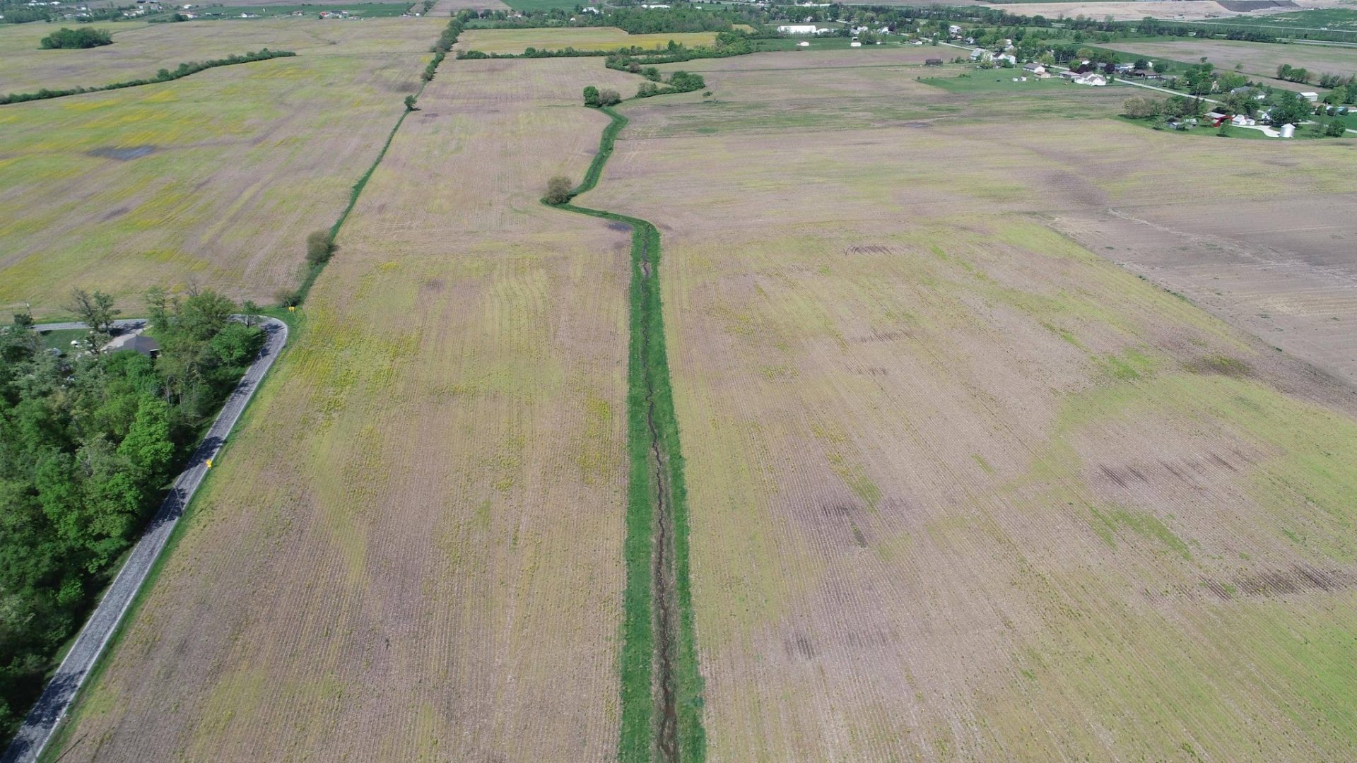 Aerial view of large, flat farm fields with a narrow green strip running through the center. Roads and trees line the edges, and scattered houses are visible in the distance. Aerial view of large, flat farm fields with a narrow green strip running through the center. Roads and trees line the edges, and scattered houses are visible in the distance.