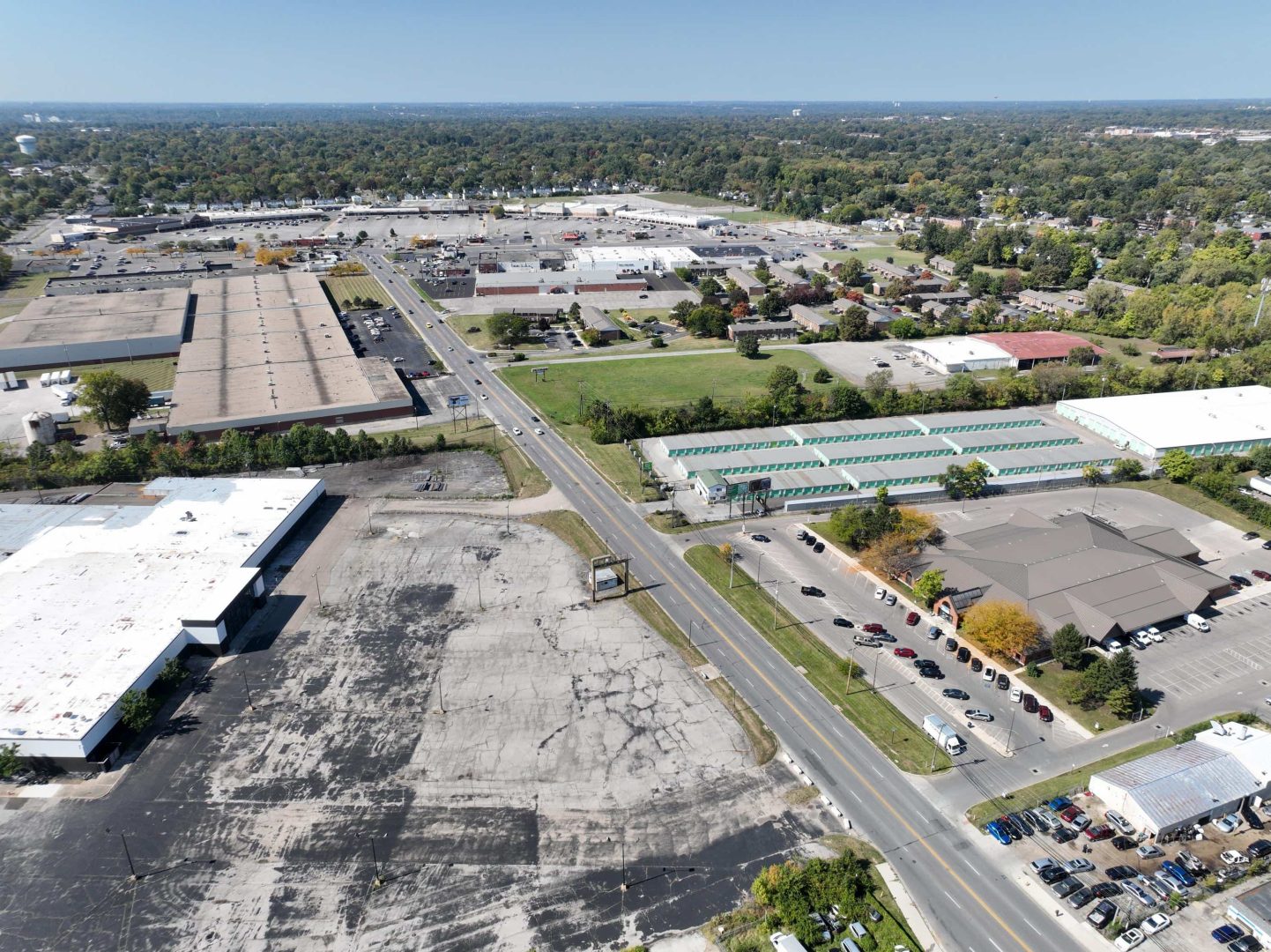 Aerial view of a commercial area with warehouses, parking lots, roads, and scattered trees. Several cars are parked, and a few drive along the main road running through the center of the image. Aerial view of a commercial area with warehouses, parking lots, roads, and scattered trees. Several cars are parked, and a few drive along the main road running through the center of the image.